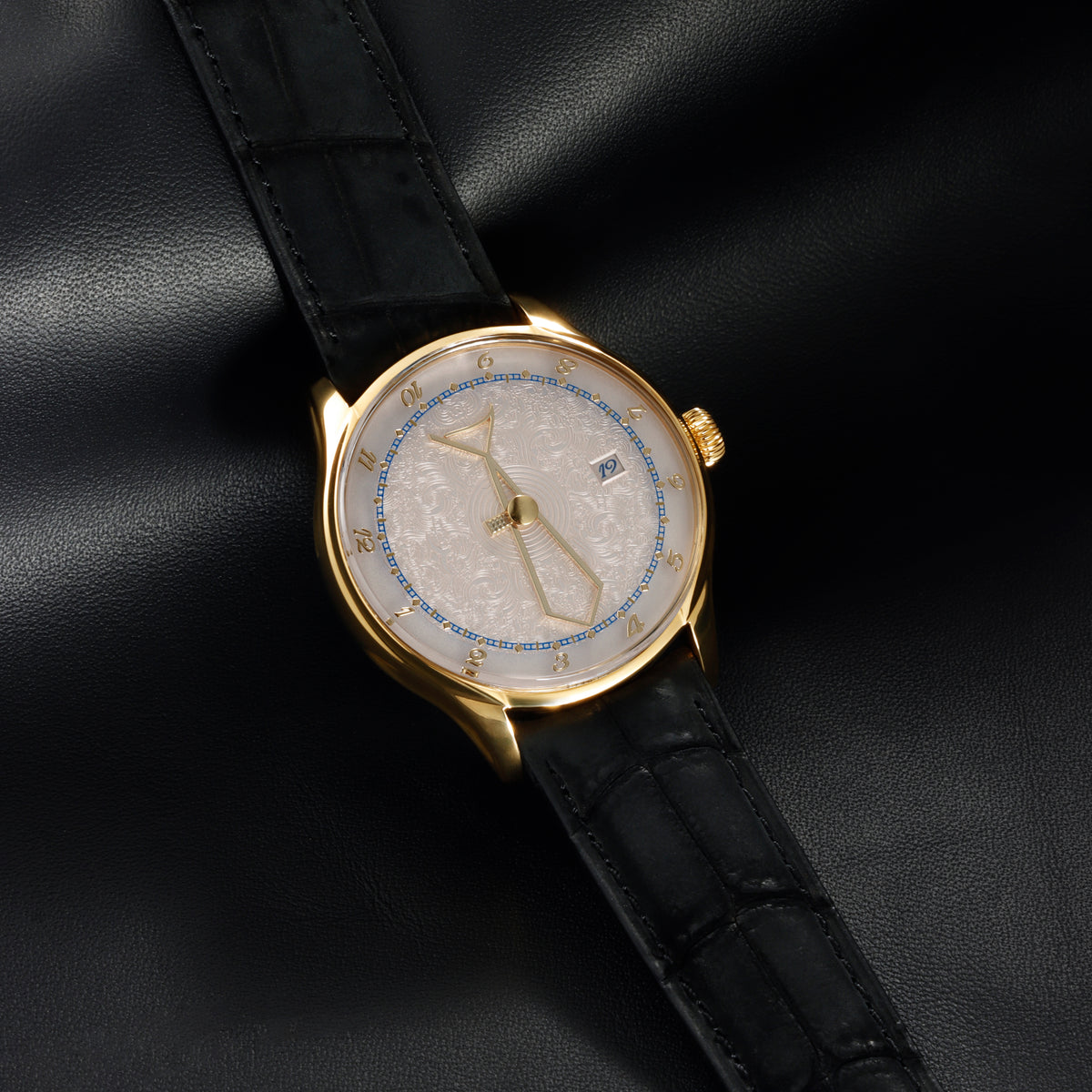 Auctor Zen tie motif hour and minute hands in PVD gold, positioned above the layered relief dial